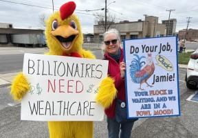 two protestors L in yellow chicken suit red comb sign Billionaires Need Wealthcare R woman in sunglasses, sign with blue edge and colorful rooster "Do your Job Jamie! Your flock is waiting an