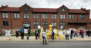 large brick historic Freight House building background. line of about 20 protestors along sidewalk in front holding signs, several dressed in chicken costumes